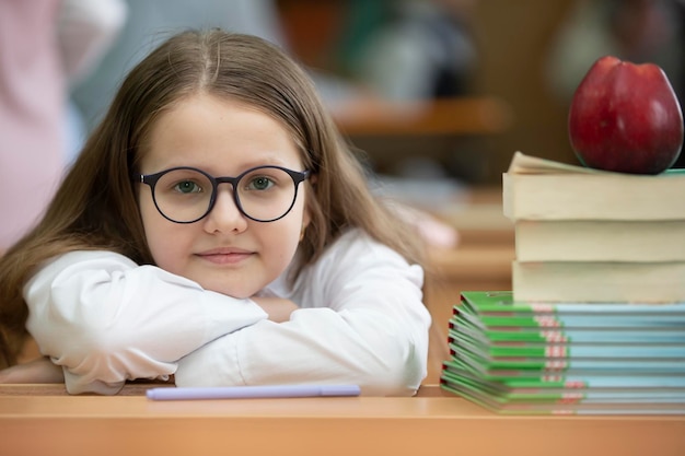 Uczennica w okularach oparła głowę na biurku Dziewczyna w klasie z książkami i jabłkiem