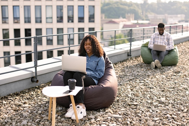 Udana kobieta biznesowa siedząca na krześle na dachu i pisząca na laptopie
