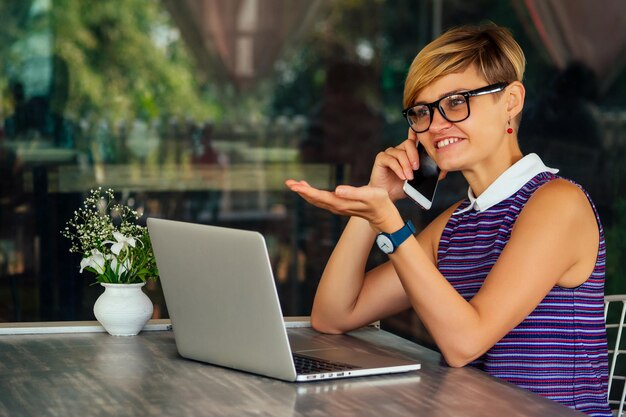 Udana młoda kobieta rozmawia przez telefon podczas przerwy na lunch. Szczery obraz bizneswoman rozmawia przez telefon w letniej kawiarni na świeżym powietrzu