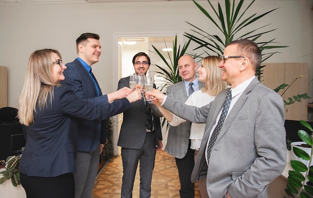 Zdjęcie udani biznesmeni trzymają kieliszki szampana i uśmiechają się, świętując w biurze.