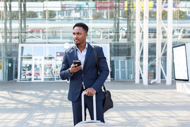 Udany młody pewny siebie African American biznesmen poruszający się z telefonem komórkowym w rękach na tle nowoczesnego biurowca w centrum miasta czarny biznesmen spacery za pomocą telefonu komórkowego w formalnym garniturze