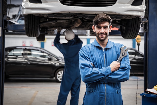 Ufna młoda mechanik pozycja z jego rękami krzyżować podczas gdy kolega z pracy pracować.