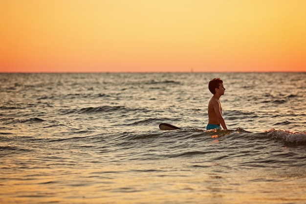 Ufny chłopiec przewożenia surfboard podczas gdy stojący przy nadmorski w zmierzchu