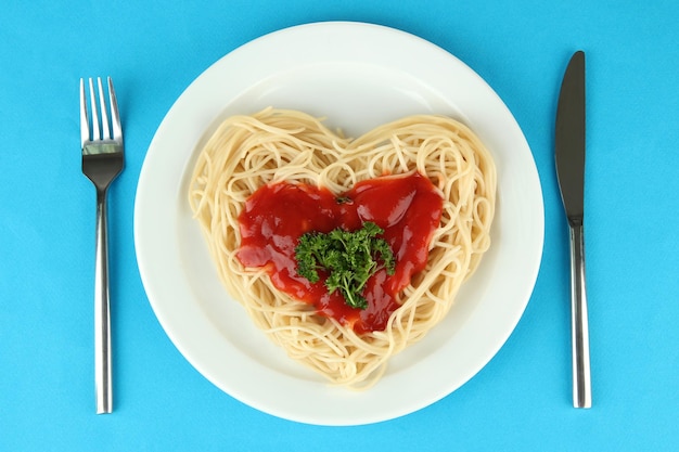 Ugotowane spaghetti starannie ułożone w kształcie serca i polane sosem pomidorowym, na kolorowym tle