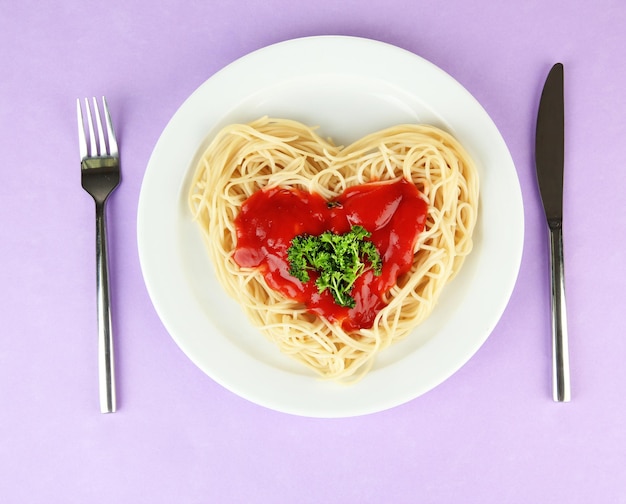 Ugotowane spaghetti starannie ułożone w kształcie serca i polane sosem pomidorowym, na kolorowym tle