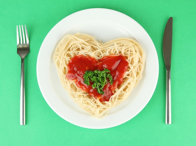 Ugotowane spaghetti starannie ułożone w kształcie serca i polane sosem pomidorowym, na kolorowym tle