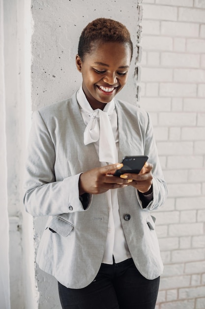 Ujęcie afrykańskiej bizneswoman korzystającej z telefonu komórkowego, gdy pochyla się nad ścianą w biurze biznes...