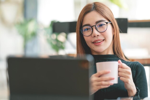 Ujęcie Atrakcyjnej Dojrzałej Bizneswoman Trzymającej Kubek I Pracującej Na Laptopie Na Swojej Stacji Roboczej