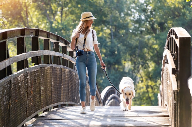 Ujęcie atrakcyjnej młodej kobiety amatorskiej fotografii spaceru z psem przez most w parku.
