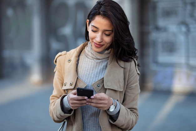 Ujęcie całkiem młodej kobiety za pomocą smartfona stojąc na ulicy.