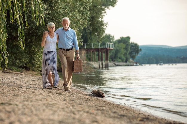 Ujęcie czułej pary seniorów idącej na piknik nad brzegiem rzeki