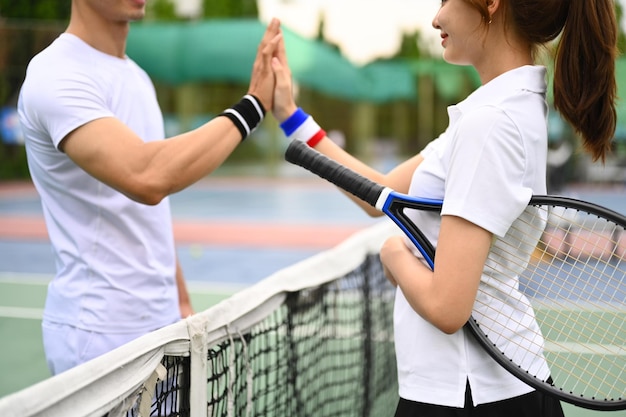 Ujęcie dwóch młodych tenisistów, którzy przybijają sobie piątkę nad siatką na korcie tenisowym