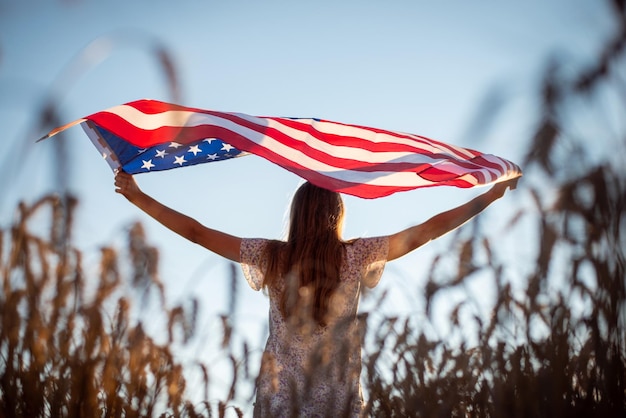 Ujęcie młodej dziewczyny z machającą flagą przed zachodzącym słońcem Dziewczyna trzymająca flagę USA