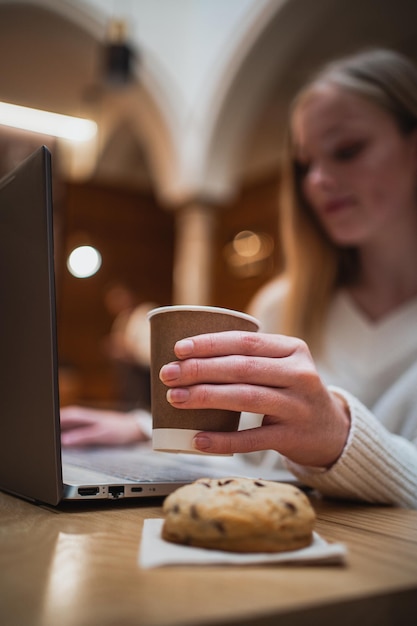 Ujęcie młodej kobiety trzymającej filiżankę gorącego cappuccino podczas pracy z komputerem