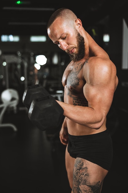 Ujęcie muskularnego kulturysty robi ciężki trening z hantlami na siłowni. Naciąga mięśnie bicepsa dużym ciężarem.