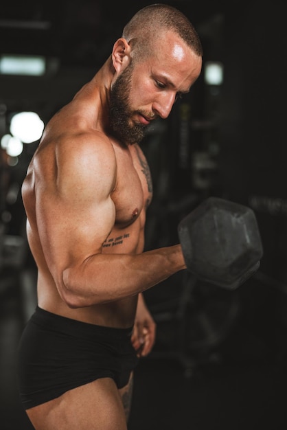 Ujęcie muskularnego kulturysty robi ciężki trening z hantlami na siłowni. Z dużym ciężarem pompuje mięsień bicepsa.