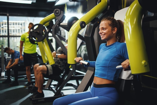 Ujęcie muskularnej młodej kobiety w sportowej pracy na treningu krzyżowym na siłowni. Ćwiczy klatkę piersiową na maszynie.