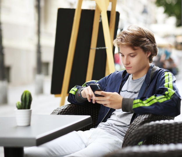 Ujęcie nastoletniego chłopca czytającego SMS-a siedzącego w kawiarni na świeżym powietrzu
