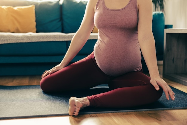 Ujęcie nie do poznania kobiety w ciąży ćwiczącej jogę w domu. Trenuje na macie do ćwiczeń i rozciąga się.