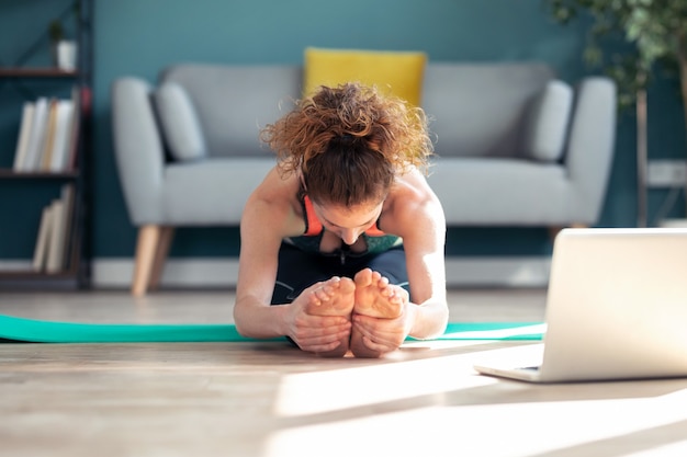 Ujęcie pewnej sportowej młodej kobiety wykonującej ćwiczenia hipopresyjne po zajęciach gimnastycznych online za pośrednictwem laptopa na podłodze w swoim salonie w domu.