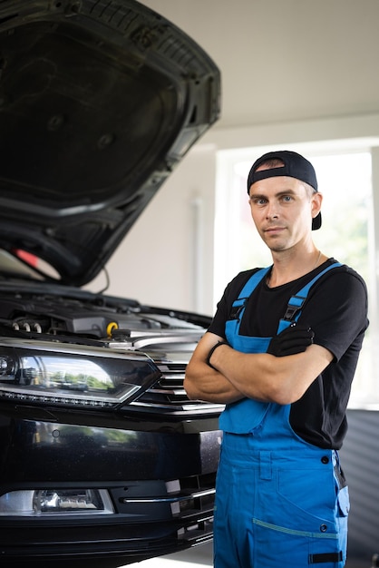 Ujęcie portretowe kaukaskiego mężczyzny w niebieskim mundurze i kapeluszu stojącego w dużym garażu samochodowym, patrzącego na kamerę