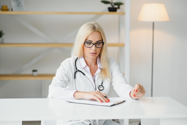 Ujęcie portretowe lekarki w średnim wieku siedzącej przy biurku i pracującej w gabinecie lekarskim