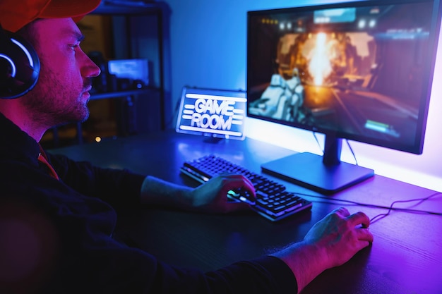Ujęcie profesjonalnego gracza grającego w strzelankę pierwszoosobową online na swoim komputerze osobistym. Pokój oświetlony neonowymi światłami w stylu Retro Arcade. Internetowe Mistrzostwa Cyber e-Sportu