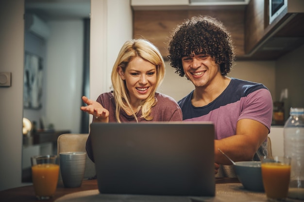 Ujęcie szczęśliwej pary razem za pomocą laptopa i jedząc śniadanie przed pracą w kuchni.