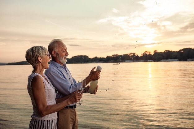 Ujęcie szczęśliwej pary seniorów pijącej szampana nad rzeką
