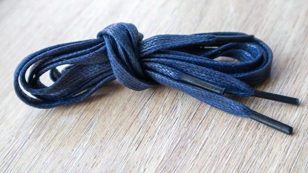Ujęcie tematyczne ciemnoniebieskich płaskich sznurówek z cienkimi końcówkami do butów podwiniętych i odizolowanych na drewnianym tle. Stylowy dodatek.