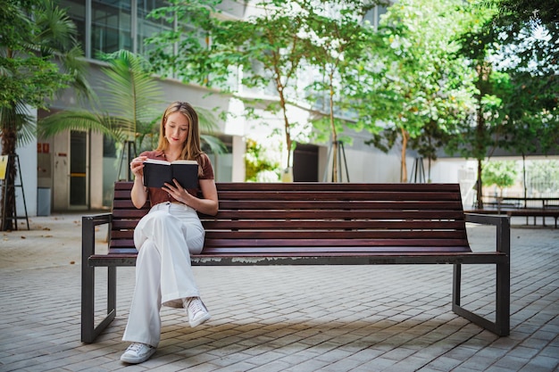 Ujęcie uspokojonej studentki czytającej książkę, gdy siedzi na ławce na kampusie uniwersyteckim