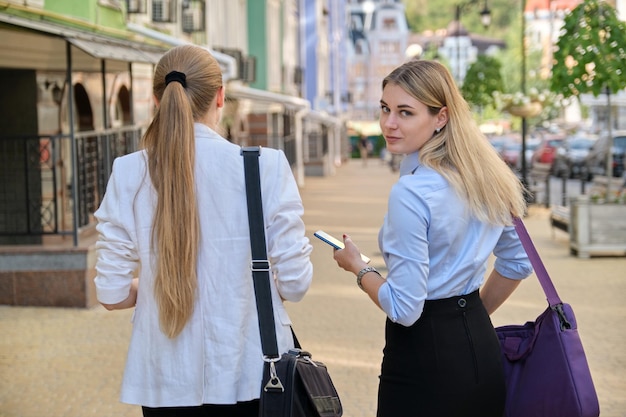 Zdjęcie ujęcie z tyłu dwóch młodych kobiet biznesu spacerujących i rozmawiających po mieście, pracownic biurowych