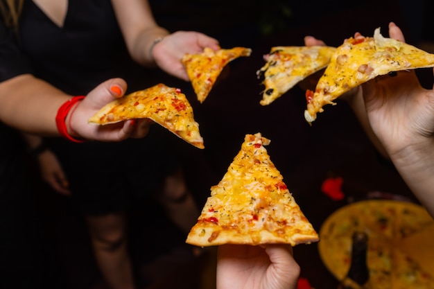 Ujęcie z wysokiego kąta grupy nierozpoznawalnych rąk ludzi, z których każdy chwyta kawałek pizzy?