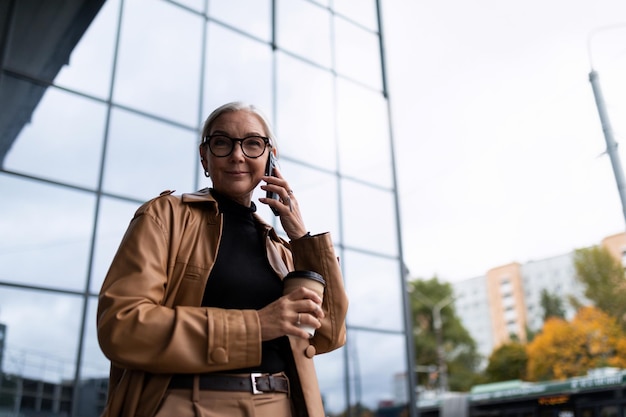 Ujmująca dorosła kobieta rozmawia przez telefon z filiżanką kawy w dłoniach