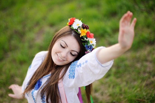 Ukrainka w koszuli i kwiatowym wianku na głowie wyciąga ręce do góry