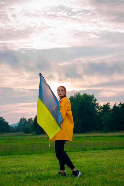 Ukrainka w polu z dużą flagą Ukrainy Patriotyczne zdjęcia Piękna kobieta w żółtym płaszczu przeciwdeszczowym