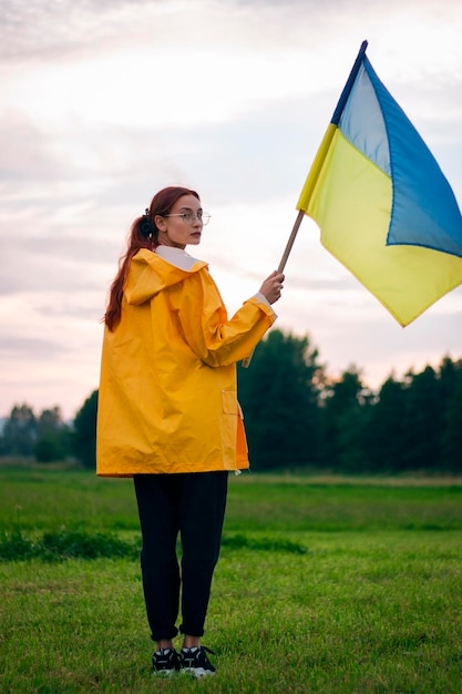 Ukrainka w polu z dużą flagą Ukrainy Patriotyczne zdjęcia Piękna kobieta w żółtym płaszczu przeciwdeszczowym