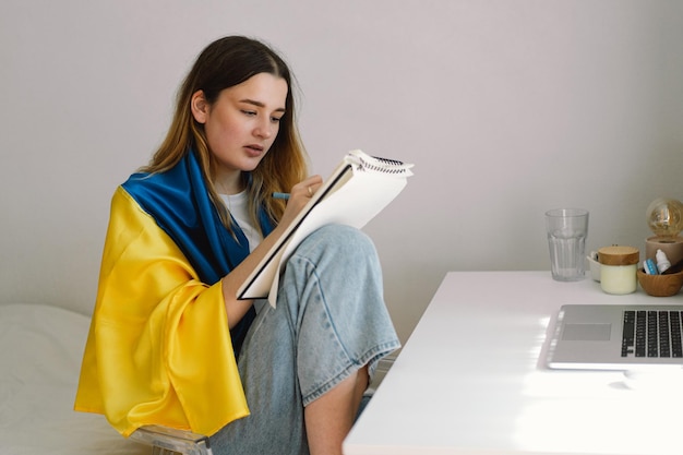 Ukraińska nastolatka owinięta w ukraińską flagę rysuje lub odrabia pracę domową w sypialni Nastolatka studiuje w domu Pojęcie studiów w czasie wojny na Ukrainie