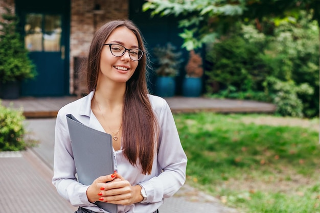 Ukraińska studentka młoda kobieta w okularach trzymająca folder uśmiechający się na tle natury