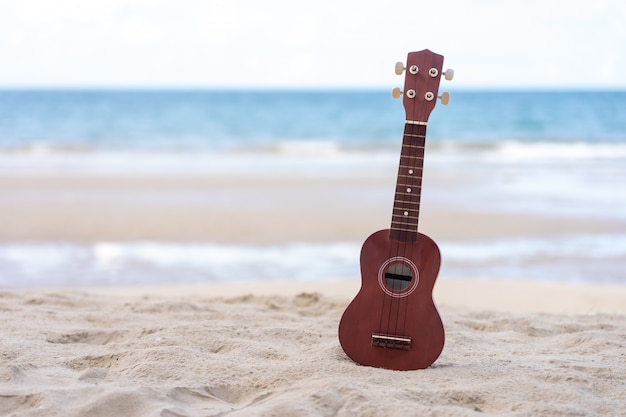 Ukulele gitary umieszczone na piaszczystej plaży. Denny widok podczas dnia z niebieskim niebem