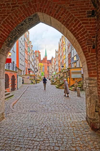 Ulica i wieże Bazyliki Najświętszej Marii Panny w starym centrum miasta w Gdańsku, Polska. Ludzie w tle