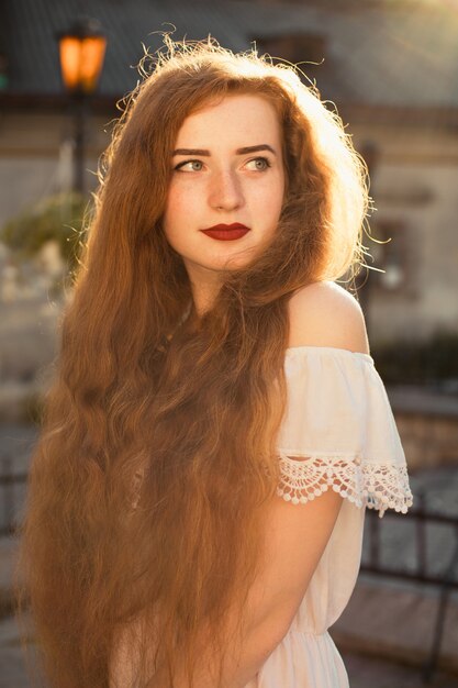Ulica portret pięknej rudowłosej modelki z kręconymi włosami pozuje wieczorem w miękkim świetle słonecznym