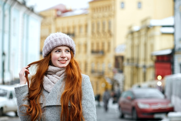 Ulica portret uśmiechający się model rude z długimi włosami na sobie ciepłą zimową odzież pozowanie na ulicy. Miejsce na tekst