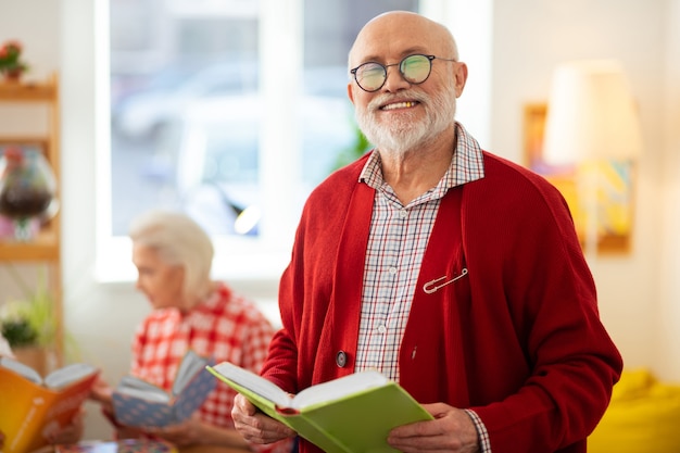 Ulubione Zajęcie. Radosny Starszy Mężczyzna Stojący Z Książką I Cieszący Się Jej Czytaniem