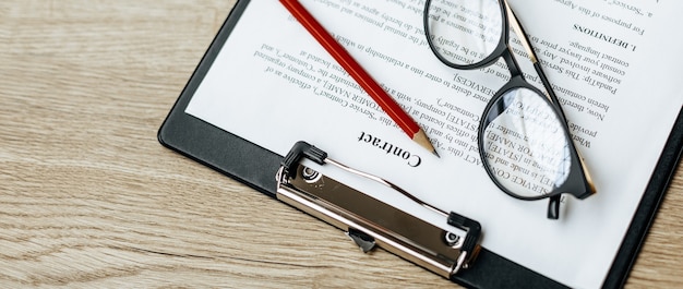 Zdjęcie umowa na drewnianym stole roboczym z okularami i czerwonym ołówkiem
