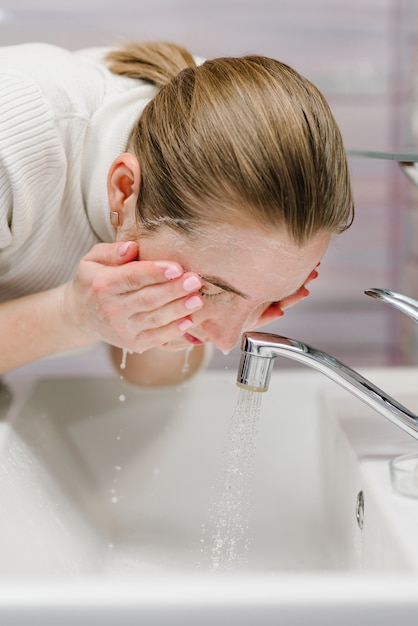 Zdjęcie umyj twarz mydłem antybakteryjnym i bieżącą wodą w zlewie. epidemiczny covid-19. zapobieganie koronawirusom. higiena ciała mydło złuszczające peeling mydło, kobieta myjąca szorowanie z pielęgnacją skóry.