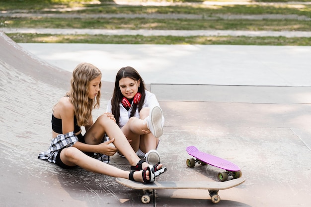 Upadek z deskorolki Aktywne dzieci dziewczyny po upadku z deskorolki ranne siedzące i pokazujące siniaki na rampie sportowej na placu zabaw w skateparku