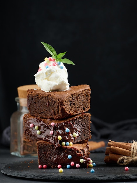 Upieczone kawałki ciasta czekoladowego brownie na czarnym stole na gałce lodów