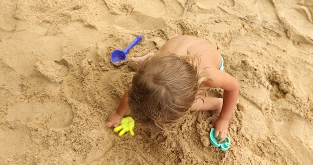 Upraw chłopiec siedzi na piaszczystej plaży tropikalnej, grając z plastikowymi zabawkami w słońcu