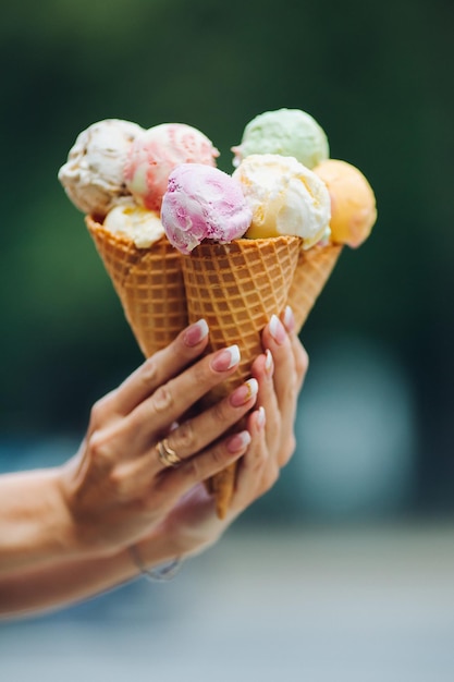Uprawa kobiecej dłoni trzymającej pyszne kolorowe lody wyglądające smacznie, słodko, pysznie, idealne na letnie upały w słoneczny dzień Ładne paznokcie z profesjonalnym francuskim manicure Koncepcja jedzenia